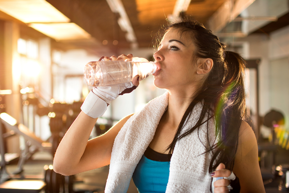 Young athletic woman drinking water in gym.